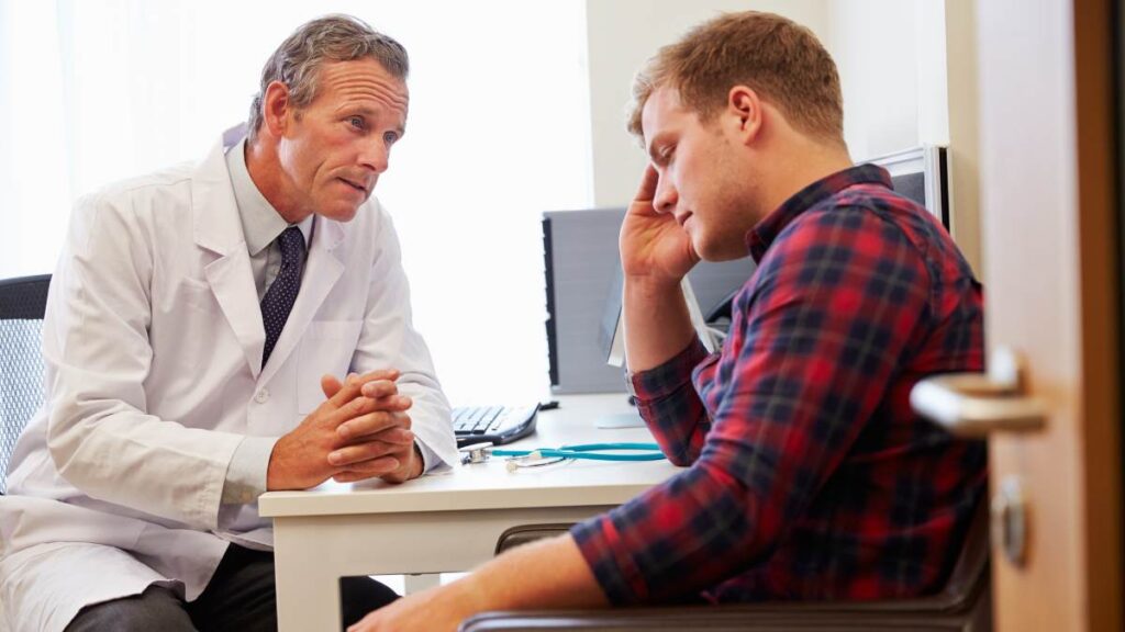 Young man struggling with addiction talking to a doctor in his office about polysubstance abuse treatment. 
